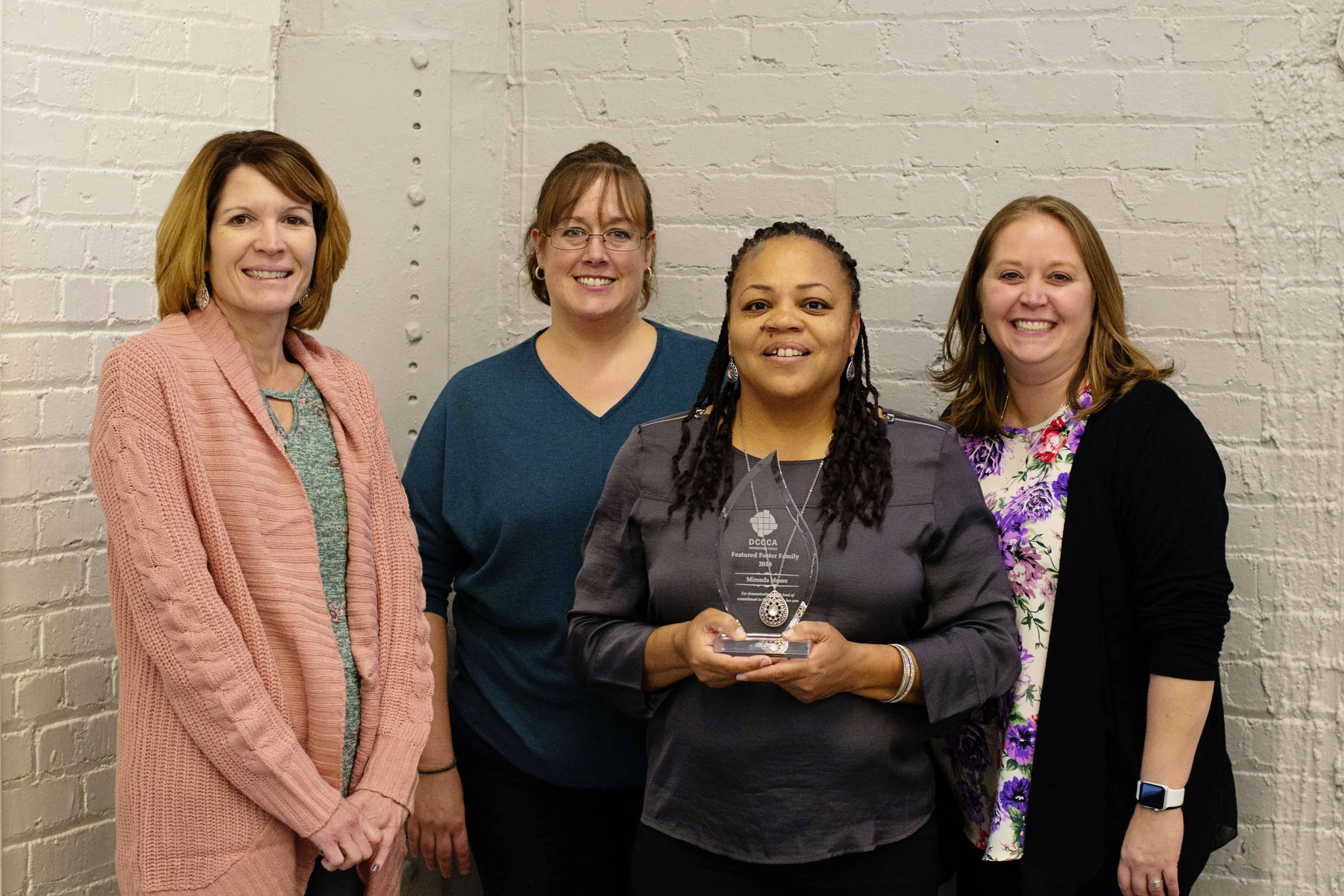 three DCCCA workers posing with a foster parent holding the featured foster family award