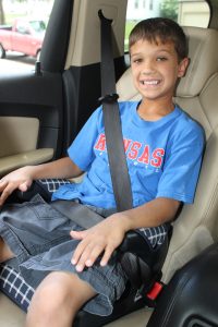 pre-teen youth smiling while sitting in a booster seat