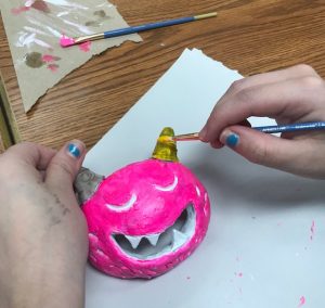 hands painting a ceramic monster mask