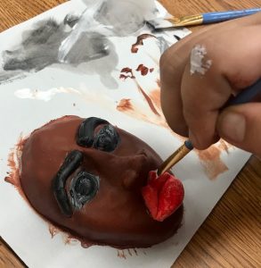 hand painting a small ceramic mask