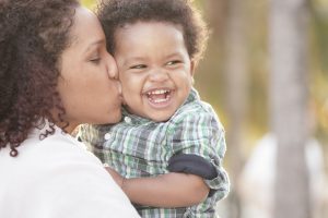 a mother holds her laughing child and kisses him on the cheek