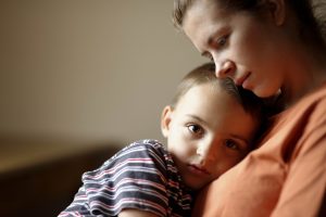 a child sits on his mother's lap and she rests her cheek on the top of his head